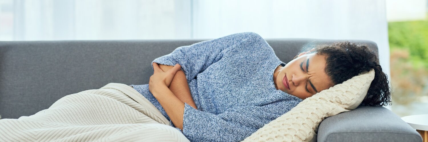 Junge Frau liegt mit Bauchkrämpfen auf dem Sofa